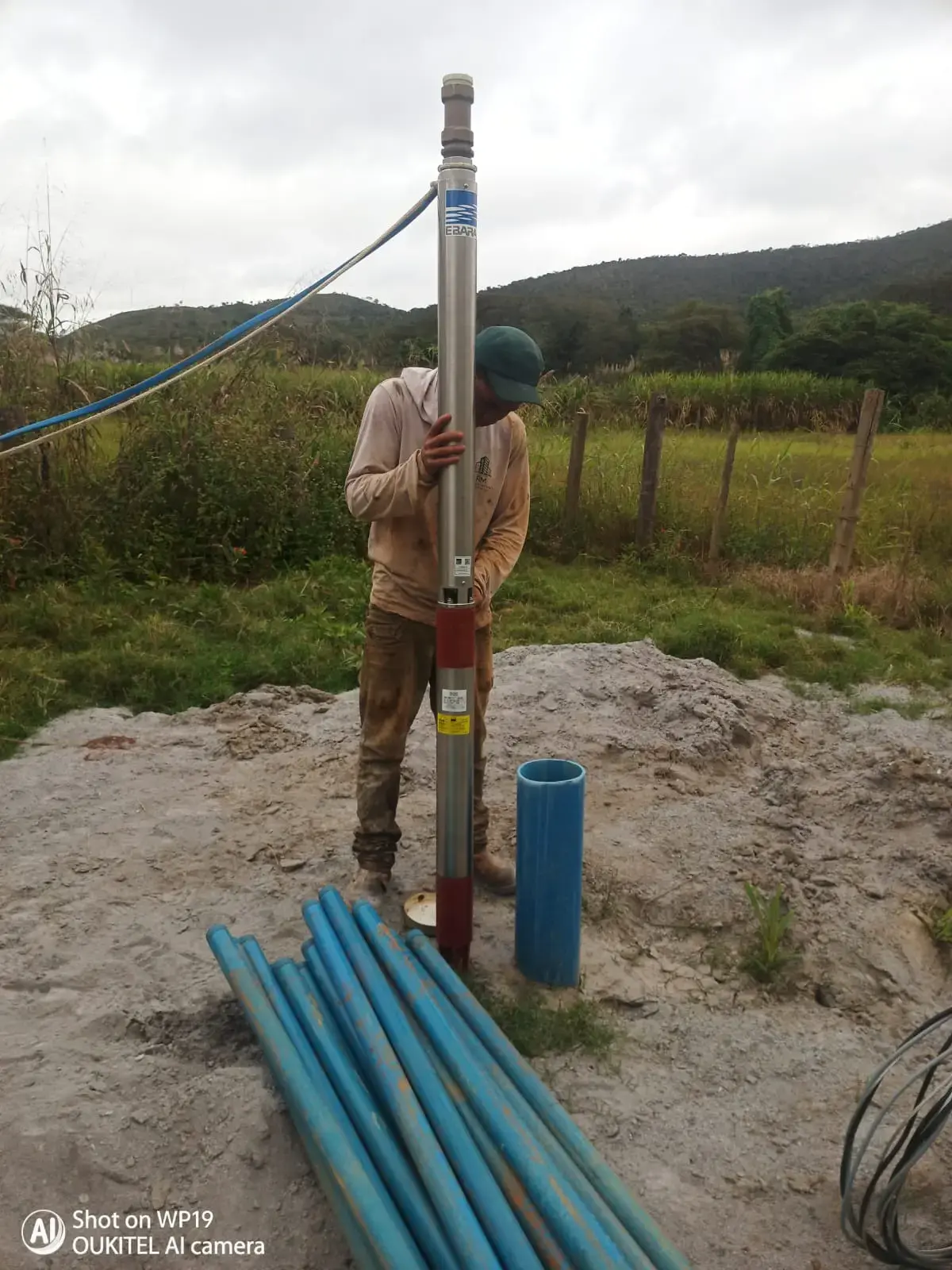 Técnico instalando bomba submersa em poço artesiano, com tubulações ao lado.