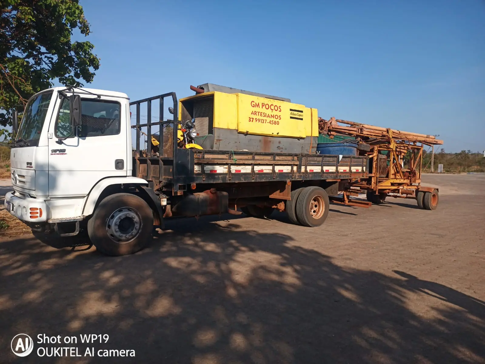 Caminhão e equipamento de perfuração da GM Poços Artesianos estacionados em terreno aberto.