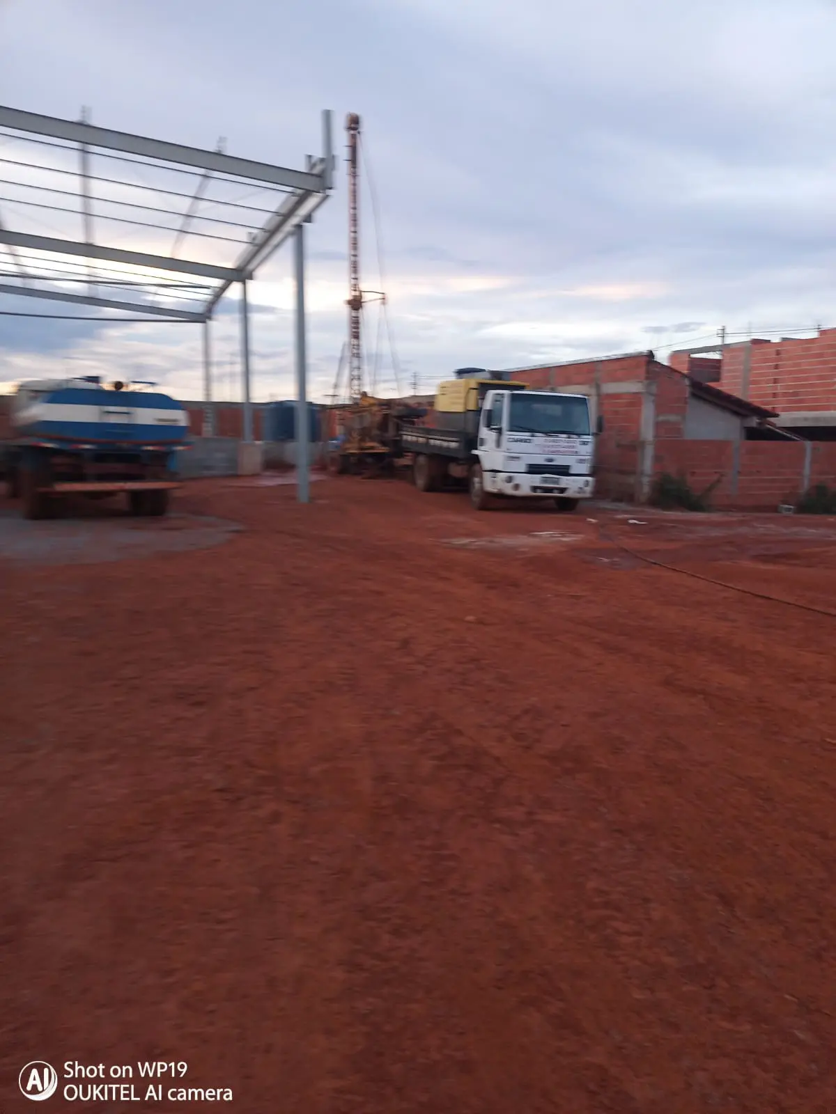 Caminhão-pipa e torre de perfuração em obra ao entardecer.